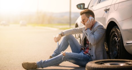 man sitting beside broken car